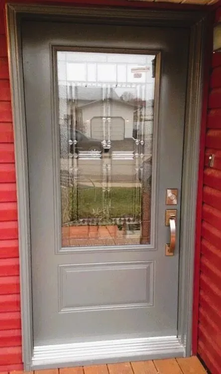 Grey entry door with decorative leaded glass on red siding in Oakville